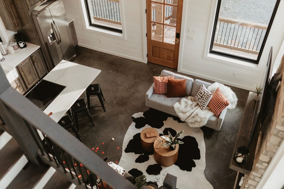 An open-concept living space with soaring ceilings, a cozy sofa, and a modern fireplace. Natural light and forest views create the perfect backdrop for gathering, relaxing, and enjoying cabin life together.