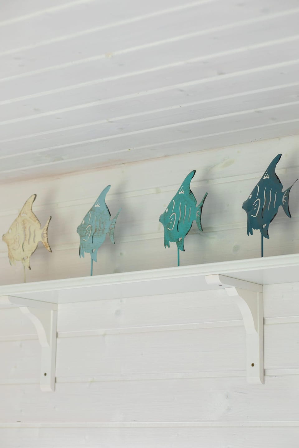 A close-up of nautical wall hooks shaped like fish, painted in blue and turquoise. Perfect for hanging coats or bags.