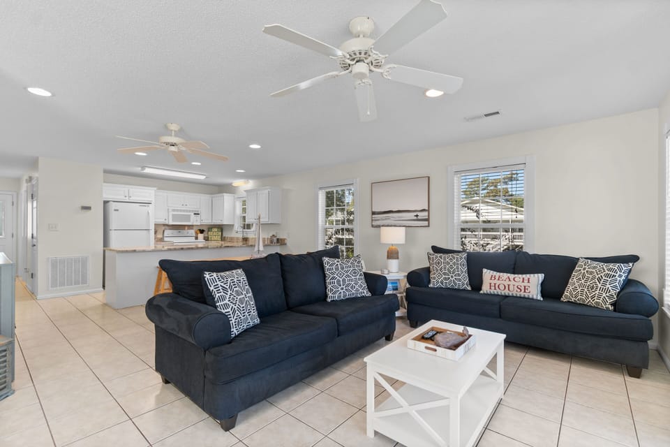 Relax in your coastal-inspired living room with plush navy sofas and open kitchen, perfectly designed for your beach getaway.