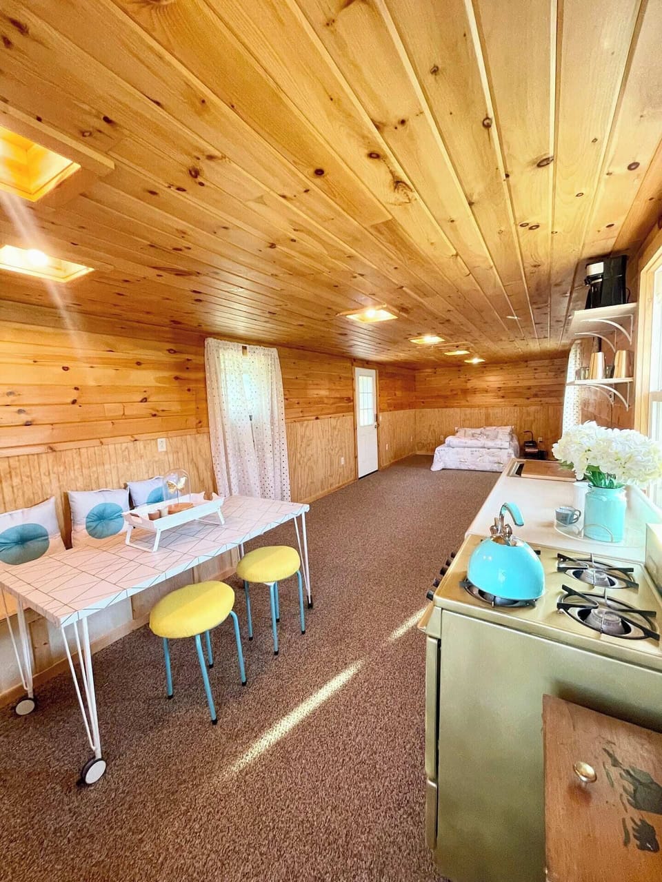 Cozy open-layout dining area with wood-paneled interior, seating for up to six, and a compact kitchen. Bright natural light and warm decor create a welcoming space for meals or relaxing indoors.