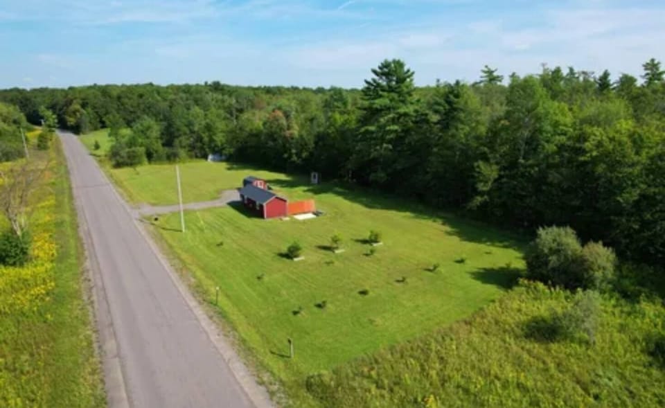 Wide aerial view of the 3 Acre Woodz property, showing the peaceful rural setting surrounded by open fields and forest.