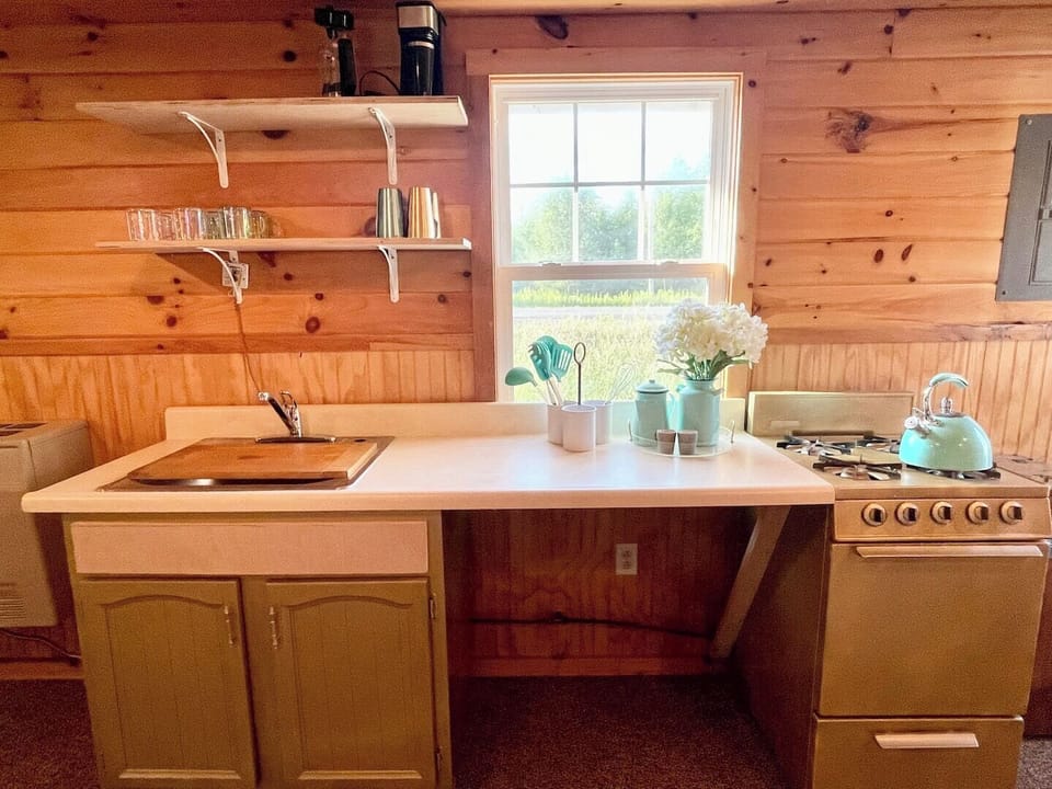 Bright kitchen with a large window for natural light, open shelving, counter space, and a sink (note: water is not currently connected; guests should bring their own supply).