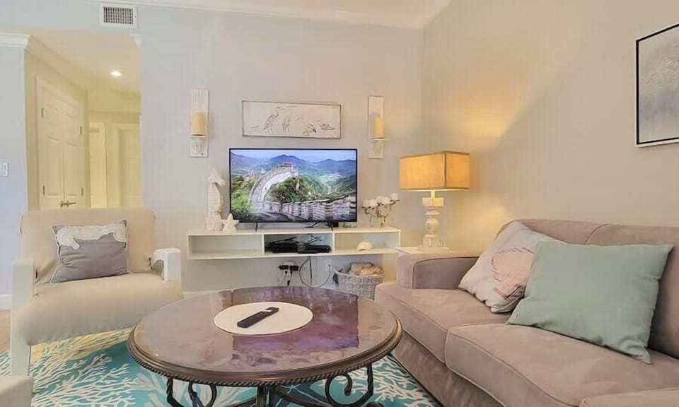Coastal‑inspired living room with soft tones, modern seating, and an open kitchen — a bright, inviting space designed for comfort and relaxation.