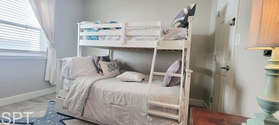 Bright coastal bunk room with soft bedding, playful beach accents, and plenty of natural light — a cozy, family‑friendly space perfect for kids or extra guests.