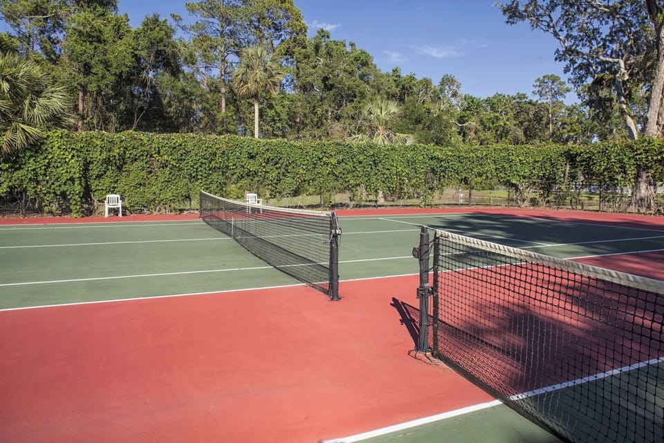 Serve up a match on sunlit courts framed by greenery.