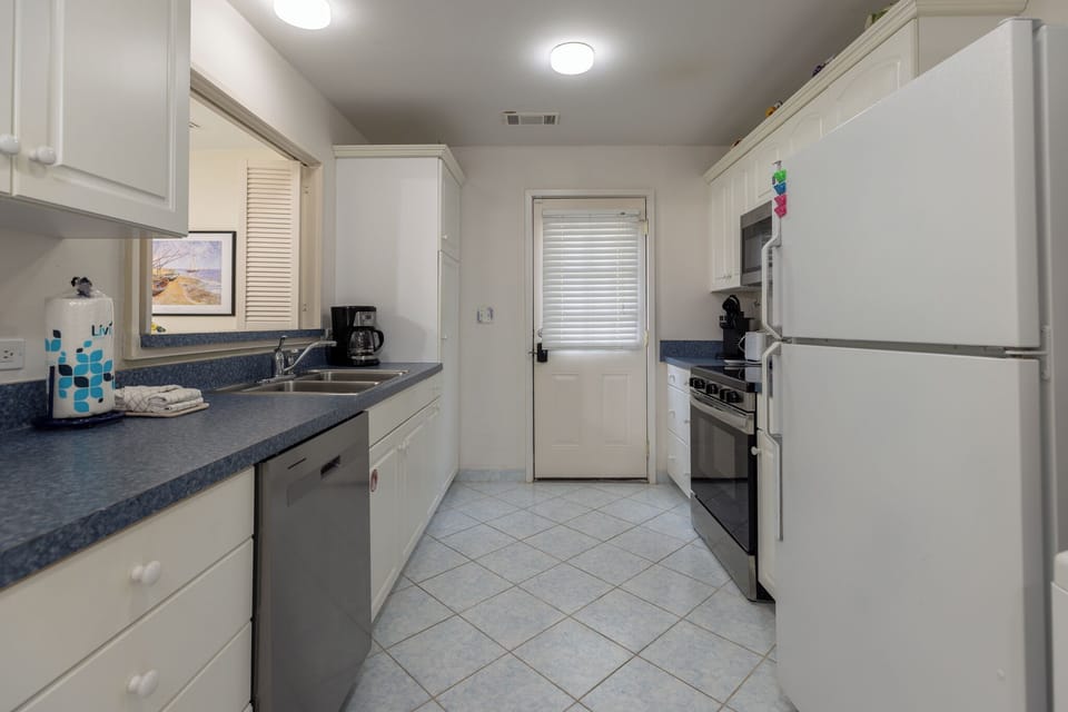 Bright galley kitchen with white cabinetry, modern appliances, and a convenient pass-through window to the dining area.