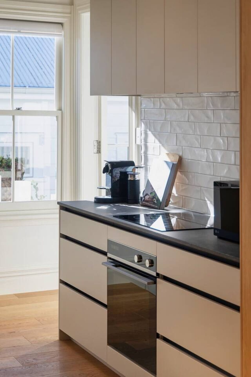 Modern fully equipped kitchen, elevated above the open plan living space, with bar seating, large fridge freezer, oven, stovetop, microwave, waste disposal, Nespresso machine, kettle and toaster