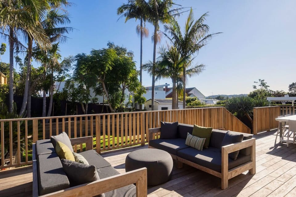Sunny deck leading off the living space, with outdoor lounge seating and dining,  and steps down to the lawn