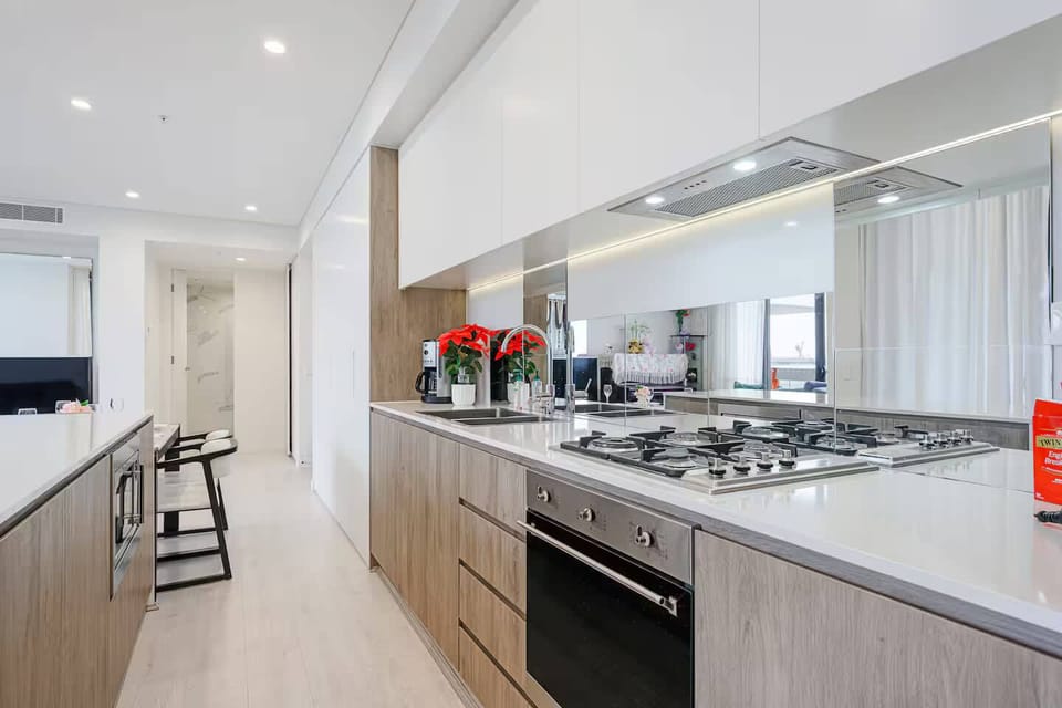 Kitchen featuring stone benchtops, gas cooktop, oven, mirrored splashback, and ample cabinetry storage.