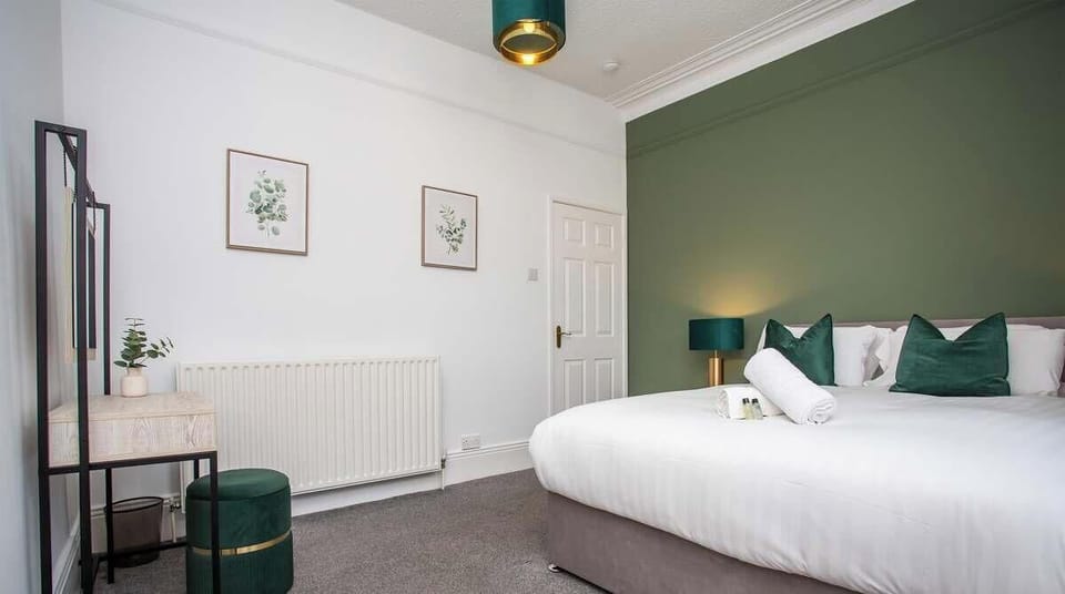 Spacious and elegant bedroom with a plush king bed, calming green feature wall, and soft ambient lighting.