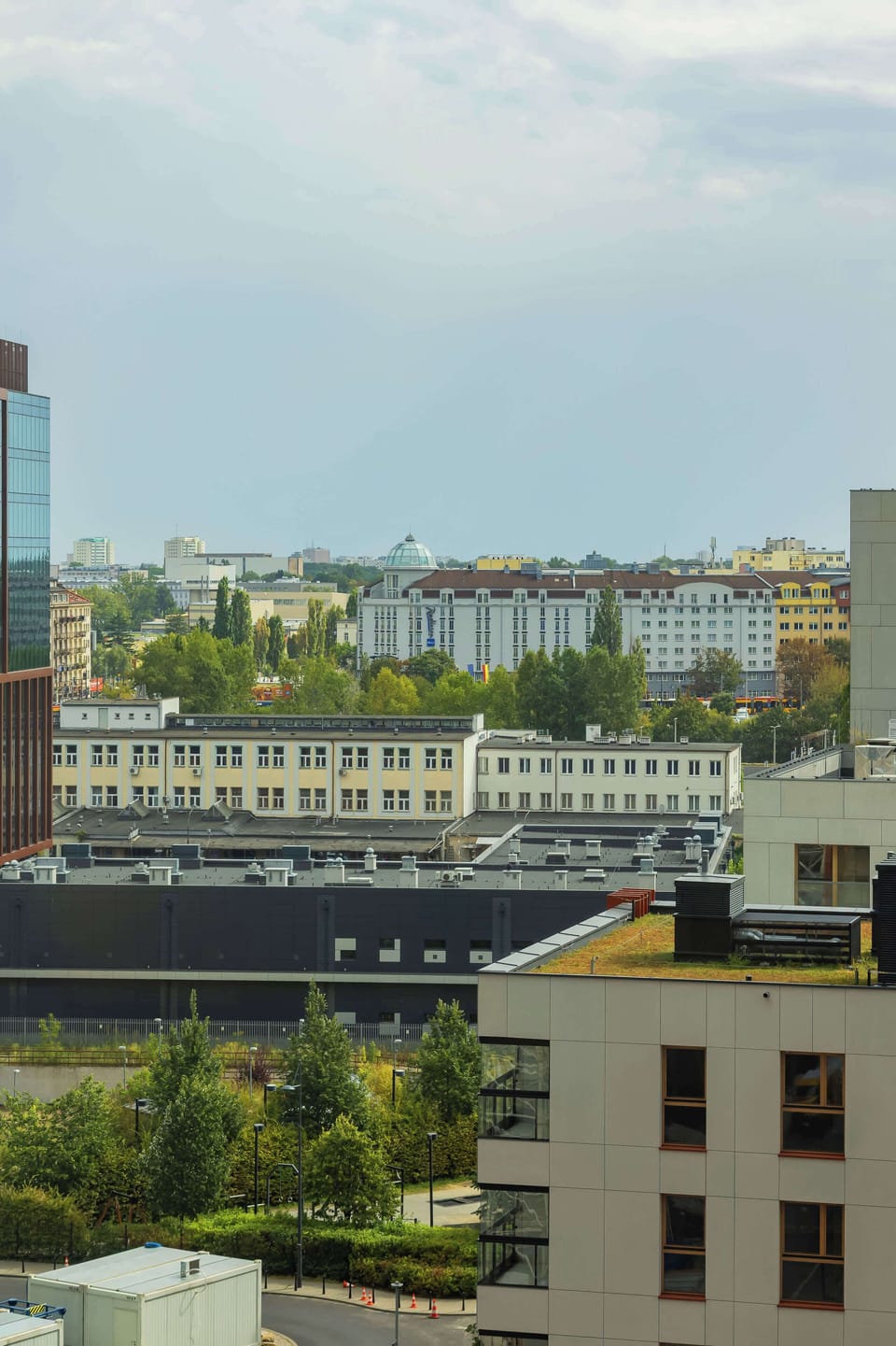 A city view taken from a higher floor of the building. Rooftops and greenery stretch out into the distance.