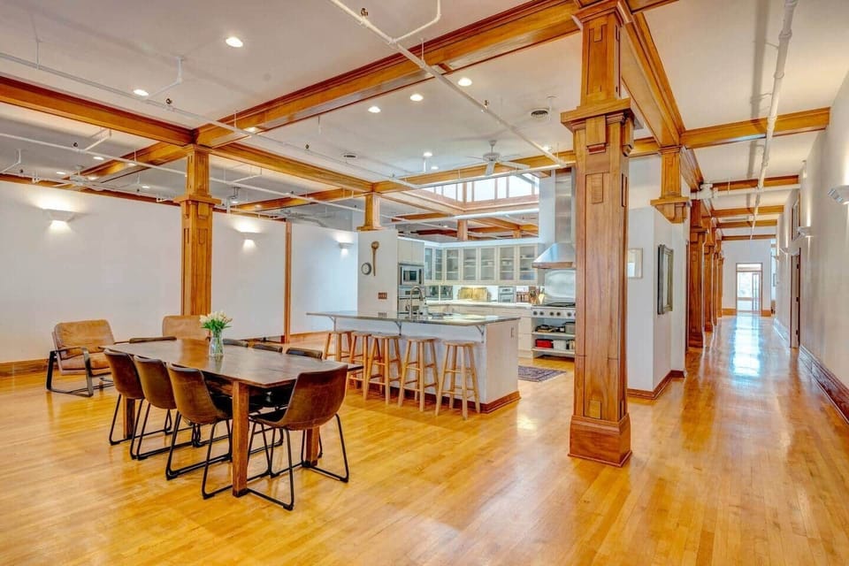 Gather in style around. dining table for eight, complemented by a kitchen island with seating for four. Towering wood columns add grandeur to the space, blending warmth and sophistication for memorable meals. 