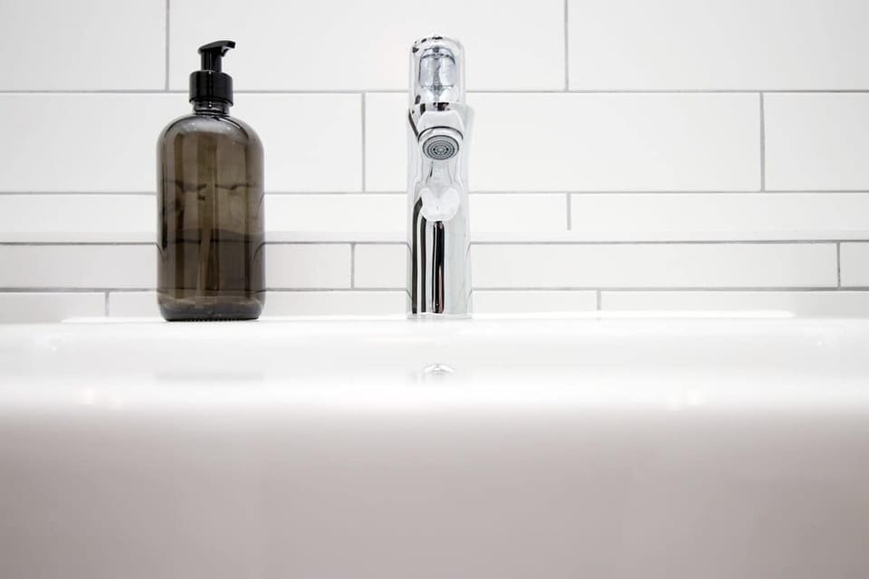 Modern, hotel-style bathroom with full bath and overhead rainfall shower. Finished with sleek fittings, fresh white tiling, and plush towels, creating a clean, relaxing space perfect for unwinding after a day out.