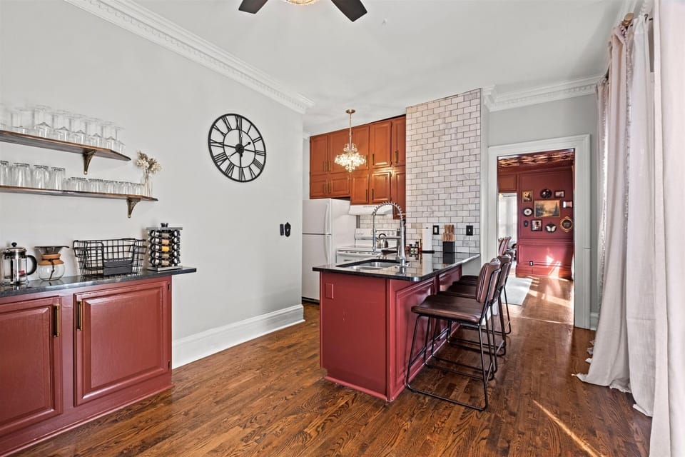 Spacious upper-level kitchen with a large island and bar seating, featuring rich cabinetry, open shelving, and hardwood floors—perfect for cooking and gathering.