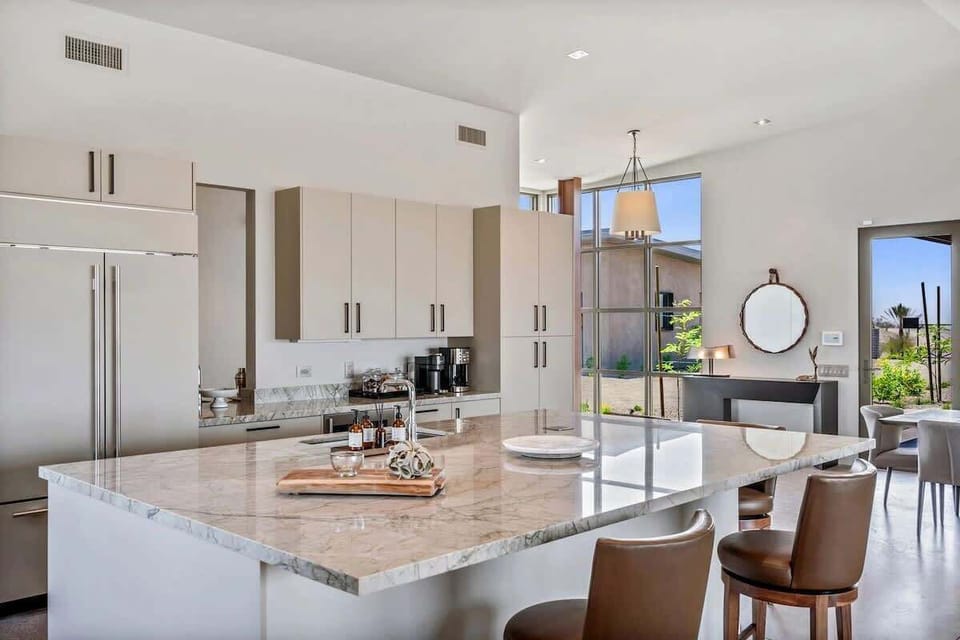 Fully equipped luxury kitchen stocked with all culinary essentials and features high-end stainless-steel appliances, a kitchen island, a dining table, and a wet bar/coffee station.