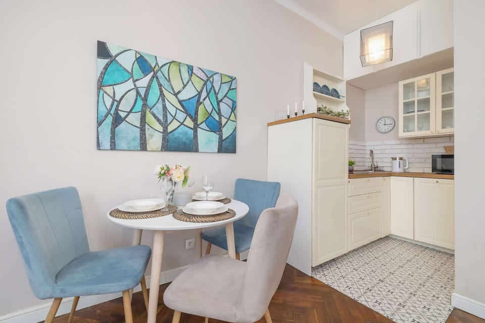 A small dining space with a round table and two turquoise chairs. The soft colors and wall art create a charming atmosphere.