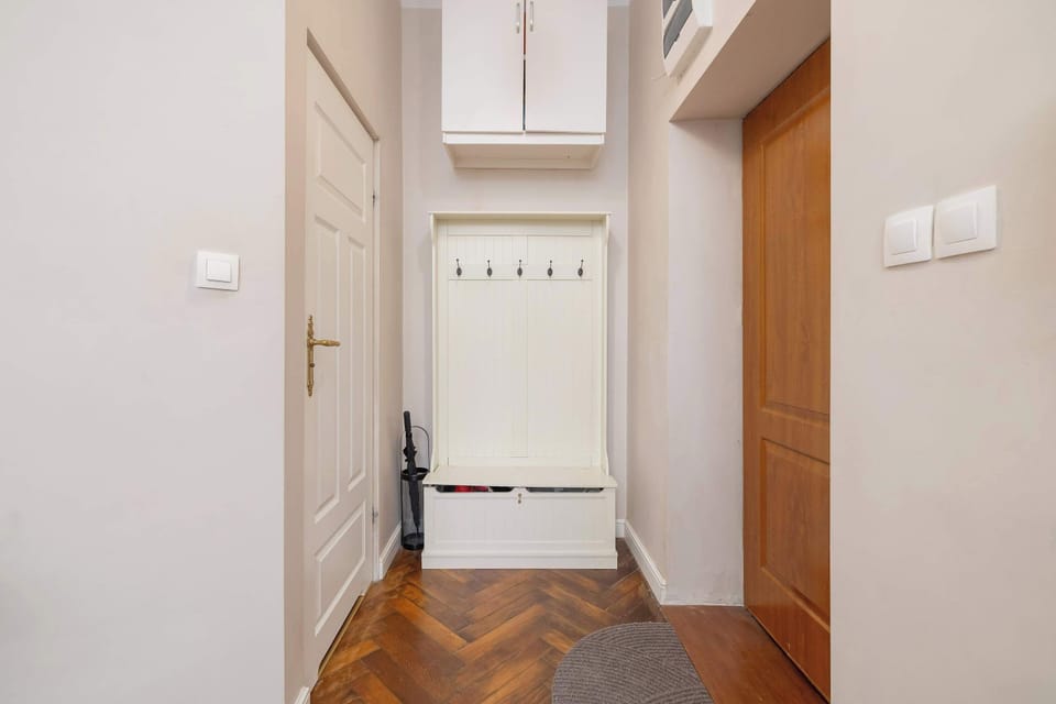 A small hallway with white walls and a wooden floor. Hooks and a bench provide practical storage for guests.