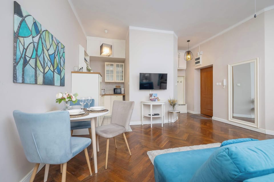 A bright living area with a dining table and TV, with a modern kitchenette in the background.