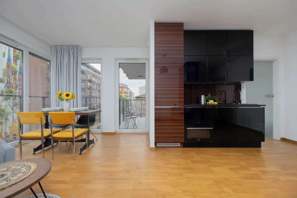 A spacious living room with a gray sofa, wooden flooring, and large windows.