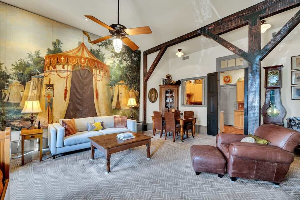This spacious living area features soaring ceilings, exposed beams, and a dramatic hand-painted mural, blending historic character with inviting comfort for a truly unique New Orleans stay.