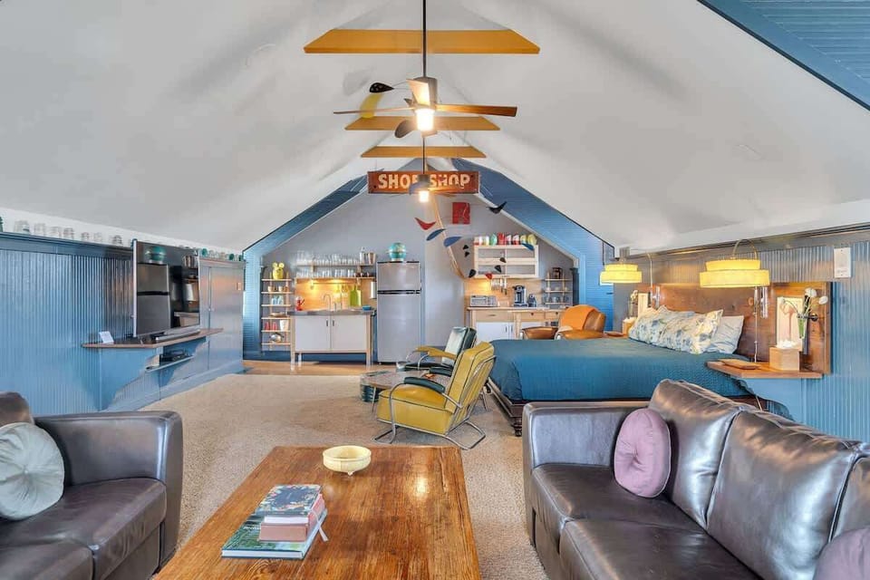 The sleeping area offers a cozy retreat with a queen bed framed by a rustic wood headboard, complemented by built-in side tables and warm, woven sconces. The vibrant teal accent wall adds character, blending comfort with a touch of eclectic charm.