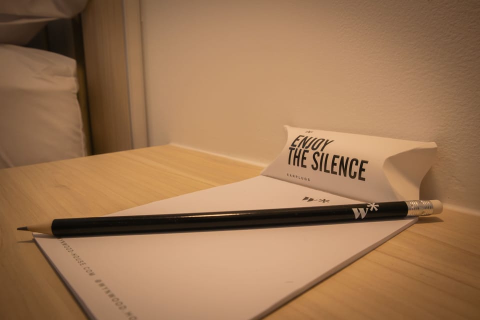 Close-up of a notepad and pencil on a wooden surface, with a paper sign that reads 'Enjoy the silence'.