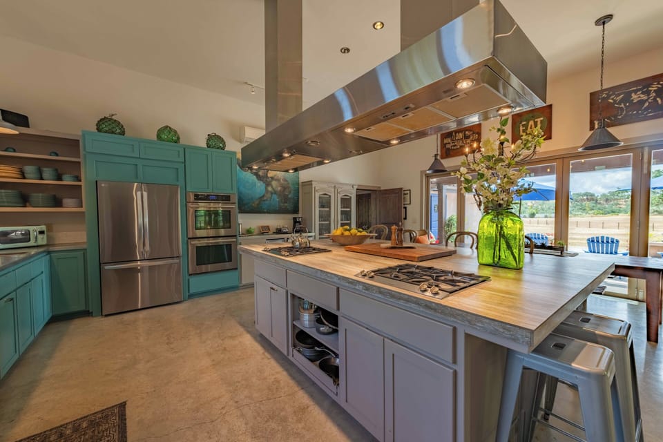 Your dream chef's kitchen awaits with beautiful turquoise cabinetry, professional gas range, spacious butcher block island, and warm natural light streaming in for inspired cooking and gathering.