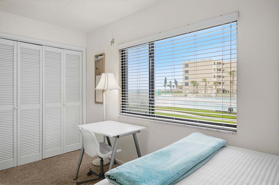 Wake up to views of the pool and ocean from this inviting guest bedroom featuring two queen beds, a dedicated workspace, and ample closet storage. A bright, comfortable retreat for a relaxing and memorable beach stay.