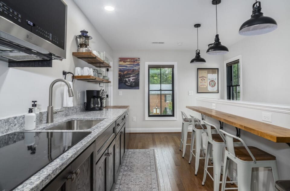 Bright and well-lit kitchen and bar style dining counter with seating for four, featuring a cooktop, apartment sized refrigerator, microwave, and cooking utensils for all your meal preparation needs.