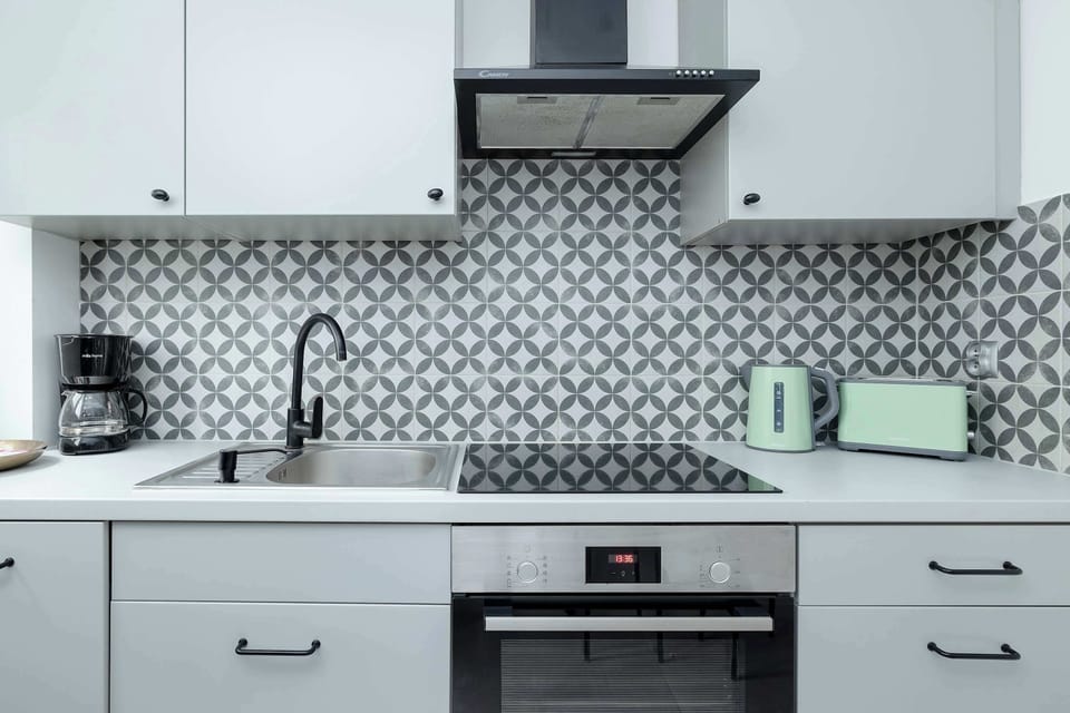 A fully equipped kitchen with white cabinets, patterned backsplash tiles, and modern appliances. A small counter space is available for meal prep.