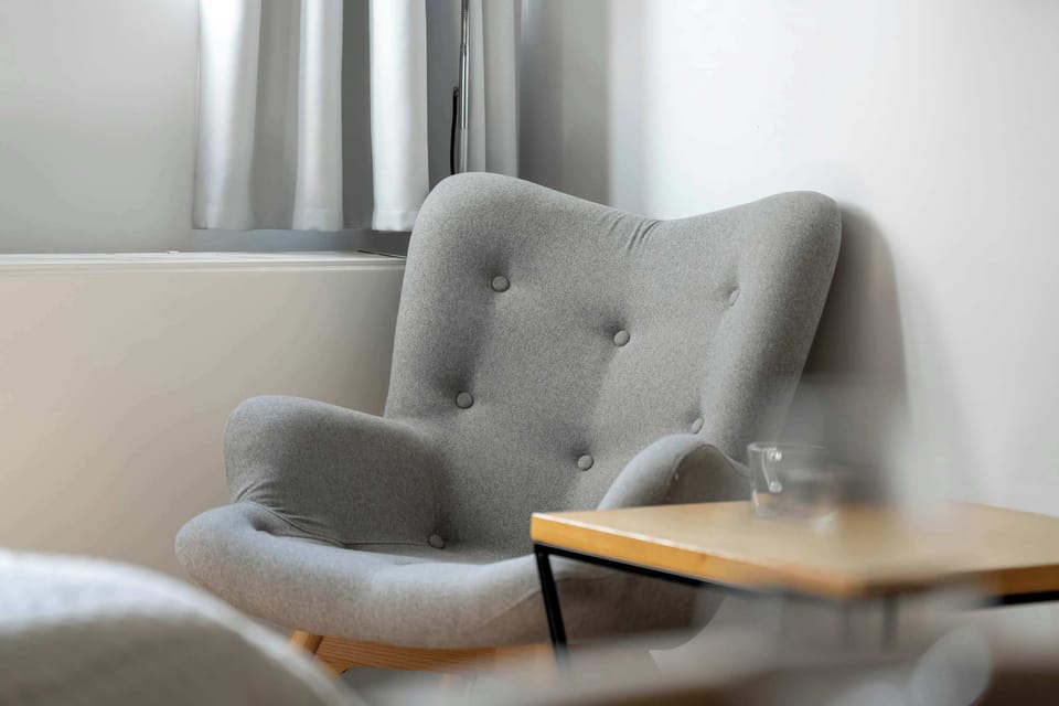 A close-up of a cozy armchair next to a small side table, perfect for reading or relaxing. The chair is upholstered in a soft grey fabric.