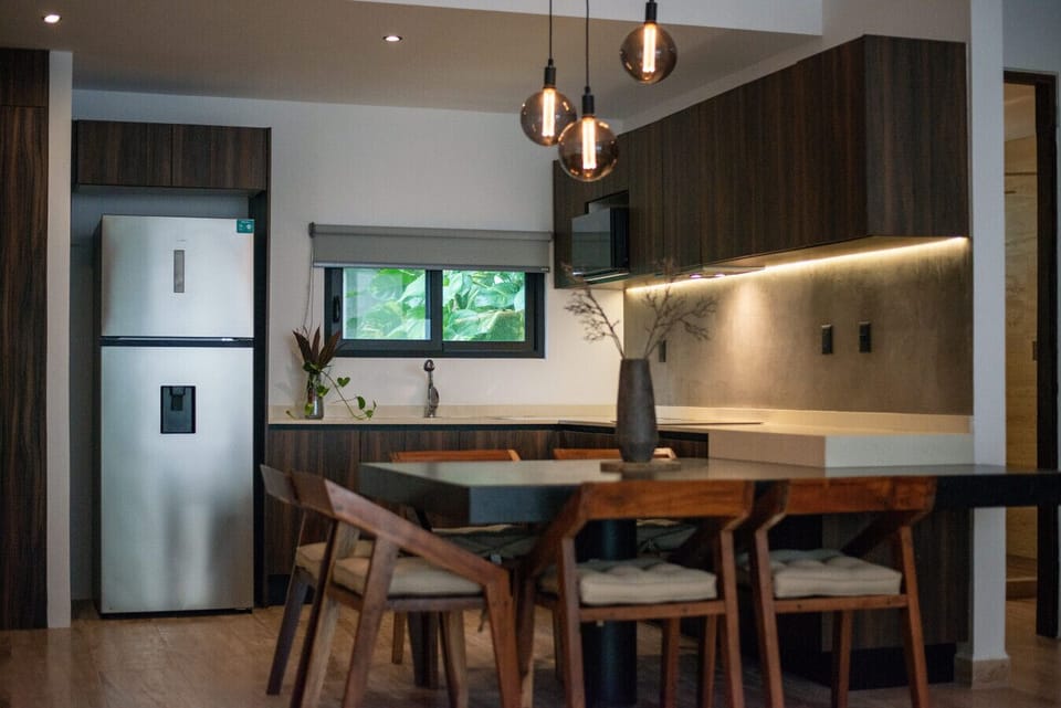 Modern kitchen with wood cabinets, black table & warm lighting.
