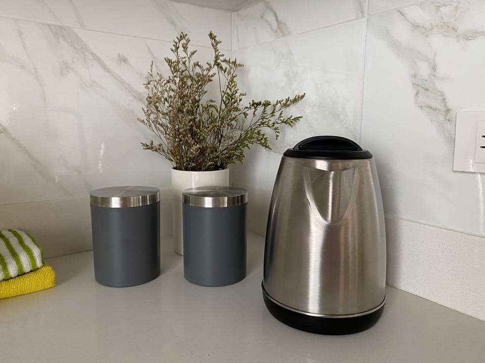 Kitchen counter setup with electric kettle, sugar and salt canisters, decorative herbs, and marble wall tiles - providing all the conveniences for tea, coffee, and cooking preparations.