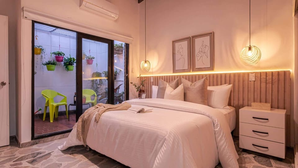 Spacious main bedroom featuring king bed, private outdoor terrace with table and chairs, full bathroom, air conditioning, modern lighting, and wall art - ideal for comfortable stays and peaceful mornings.