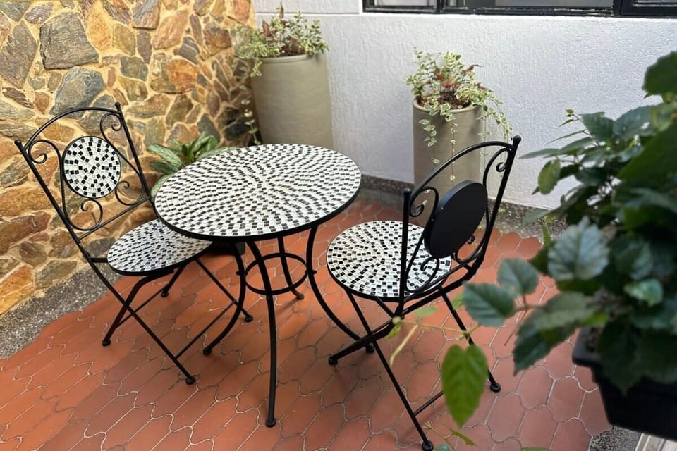 Private outdoor terrace with decorative mosaic table, elegant iron seating, stone accent wall, and greenery - ideal for morning coffee, alfresco dining, and enjoying fresh air moments.