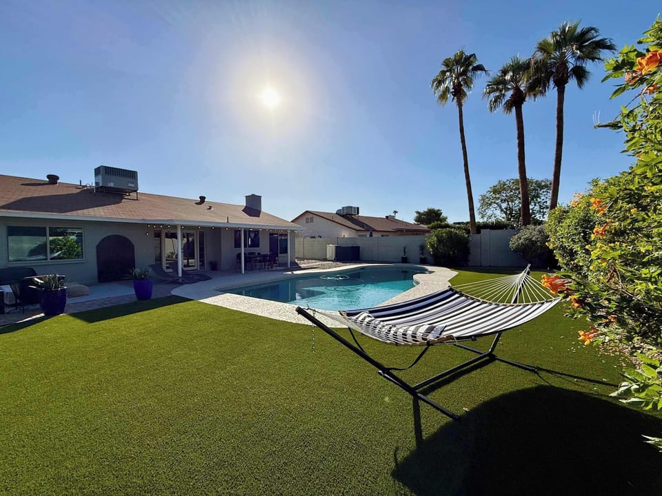 Relax in the hammock overlooking the updated pool, palm trees, and modern turf yard, ideal for lazy afternoons or sunset lounging.