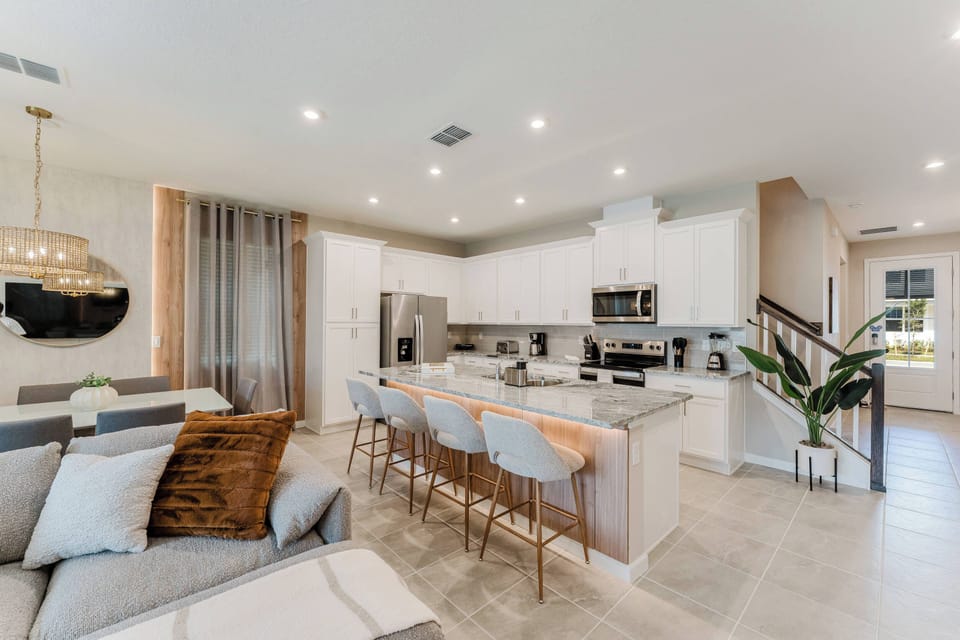 Welcome to a stylish kitchen with chic bar stools around the island, where soft recessed lighting enhances sleek white cabinetry and elegant countertops, creating the perfect atmosphere for your culinary adventures.
