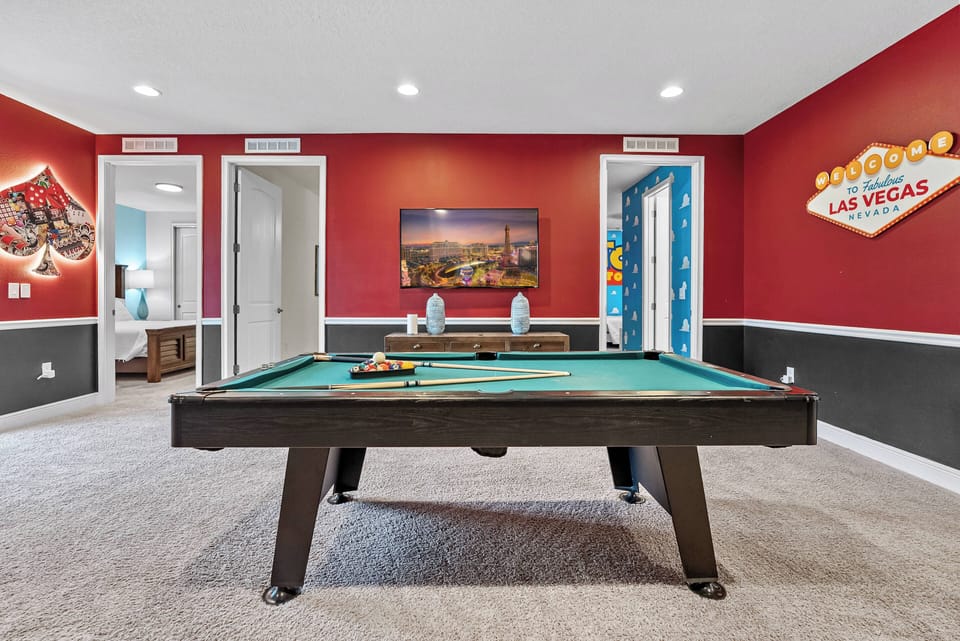 Step into a vibrant game room featuring a classic billiard table that promises fun-filled evenings. The striking red walls, accented by playful decor, create an energetic atmosphere perfect for both relaxation and entertainment.
