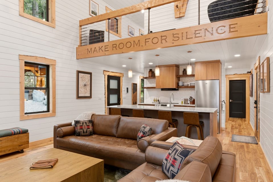An open-concept living space designed for connection — featuring a gas fireplace, mid-century furnishings, and the signature “Make Room for Silence” beam.