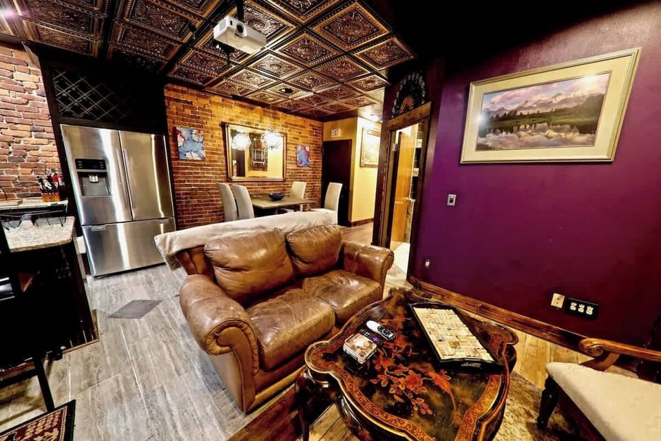 View from the projector screen shows the dining area and highlights the lighting in the space. Purples, gold, and vintage brick are iluminated and highlighted by the sold white glow of the overheads and chandelier over the dining table.