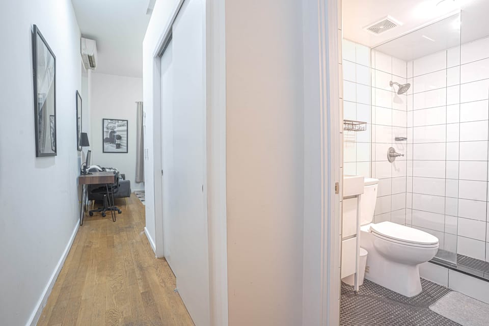 Hallway with workspace nook leading to modern bathroom and bedroom, accented by wood flooring.