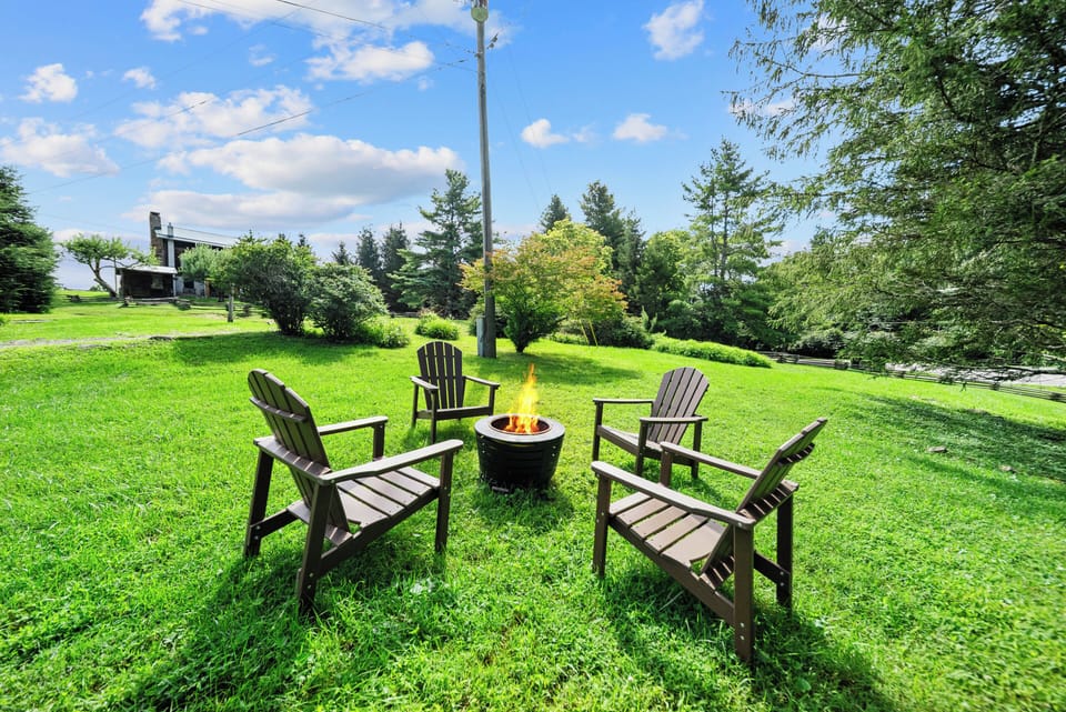 Gather around the fire pit on the open lawn, with the cozy log cabin nestled among the trees just steps away.