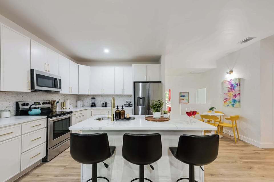 Bright modern kitchen with white cabinets, stainless steel appliances, and a central island with black barstools perfect for gathering.
