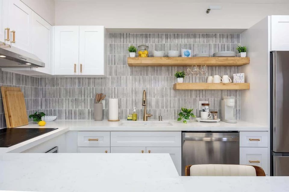 Prepare meals with ease in this well-appointed kitchen, featuring a sleek dishwasher, gold-accented faucet, and open shelving stocked with dinnerware and glasses.