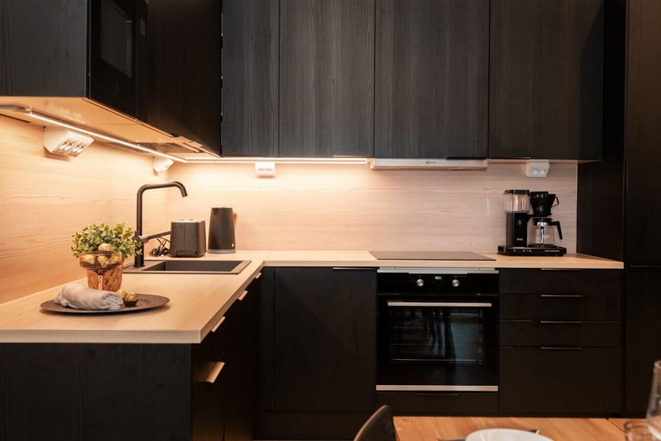 Prepare your favorite meals in this sleek, fully-equipped kitchen, featuring modern black cabinetry, integrated appliances, and warm under-cabinet lighting.