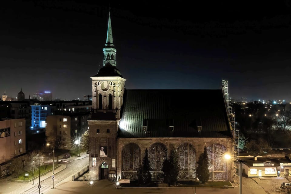 A church at night with its green roof illuminated by spotlights. The tower dominates the skyline.