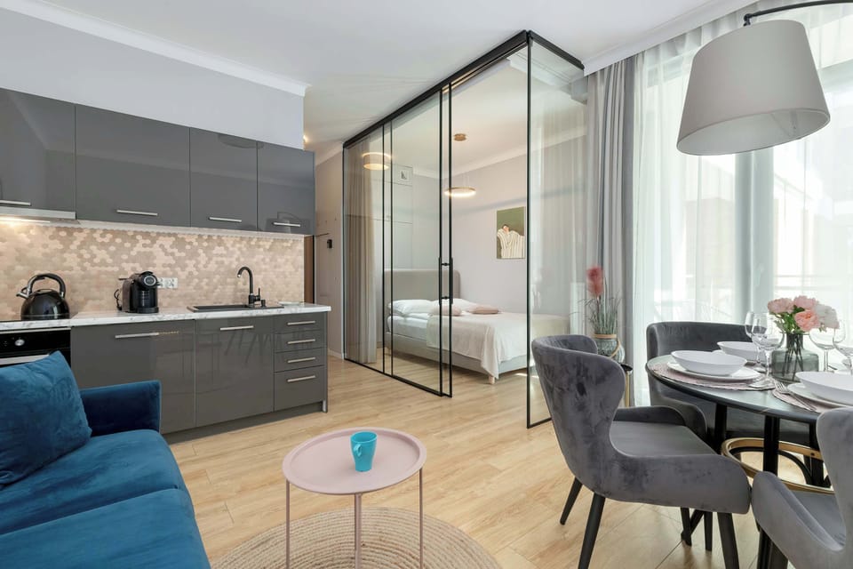 Another angle of the living room with a sofa, a dining table, and open kitchen. Large windows bring in natural light.