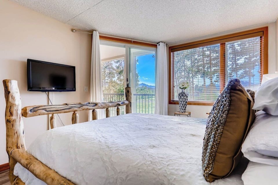 Enjoy serene mountain views from the cozy warmth of your bedroom, featuring a rustic wood bed frame and direct access to a private balcony.