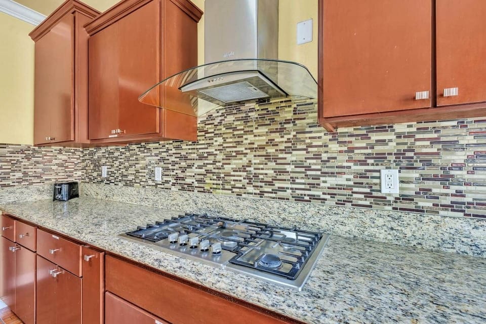 5-burner gas stove with range hood, set against a mosaic backsplash and granite counters.