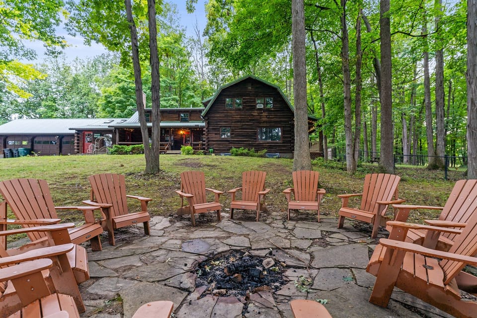 Gather around the fire pit under towering trees, complete with Adirondack chairs and a serene view of the lake in the distance.